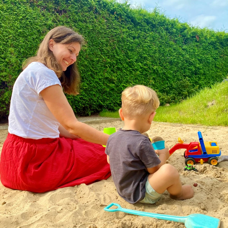 Tgesmutter sitzt mit Kind im Sandkasten
