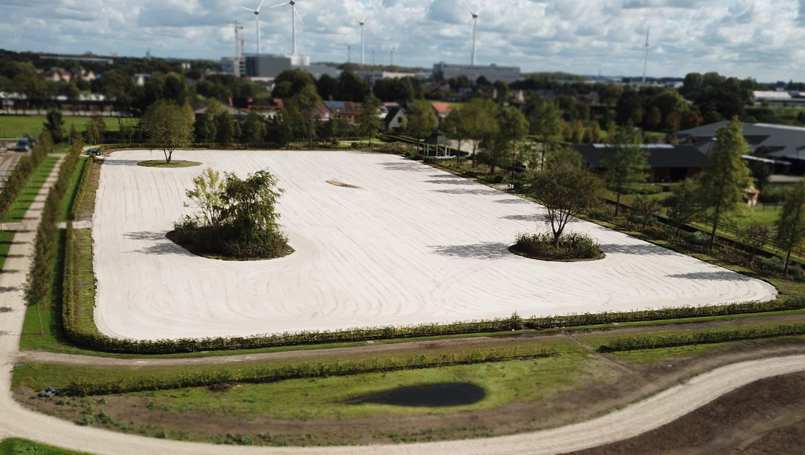 Aanleg van professionele graspiste met wit zandbed, omringd door groenvoorziening en waterbuffer, ideaal voor drainage en bodemstabiliteit