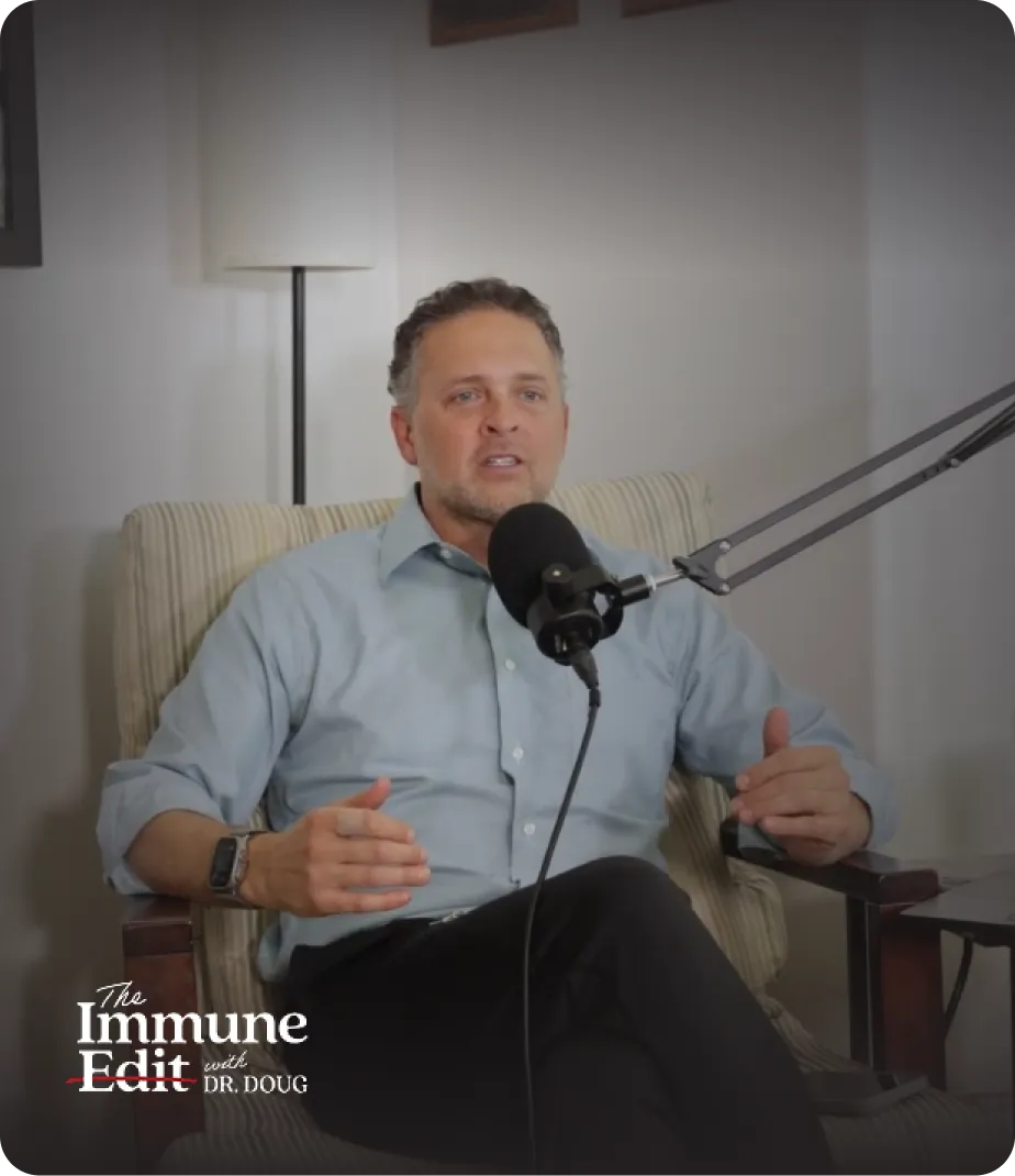 Man in a light blue shirt speaking into a microphone while seated in a striped armchair during a podcast.