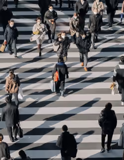 Menschen in Mänteln und Masken, die eine breite, gestreifte Zebrastreifen-Straße überqueren.