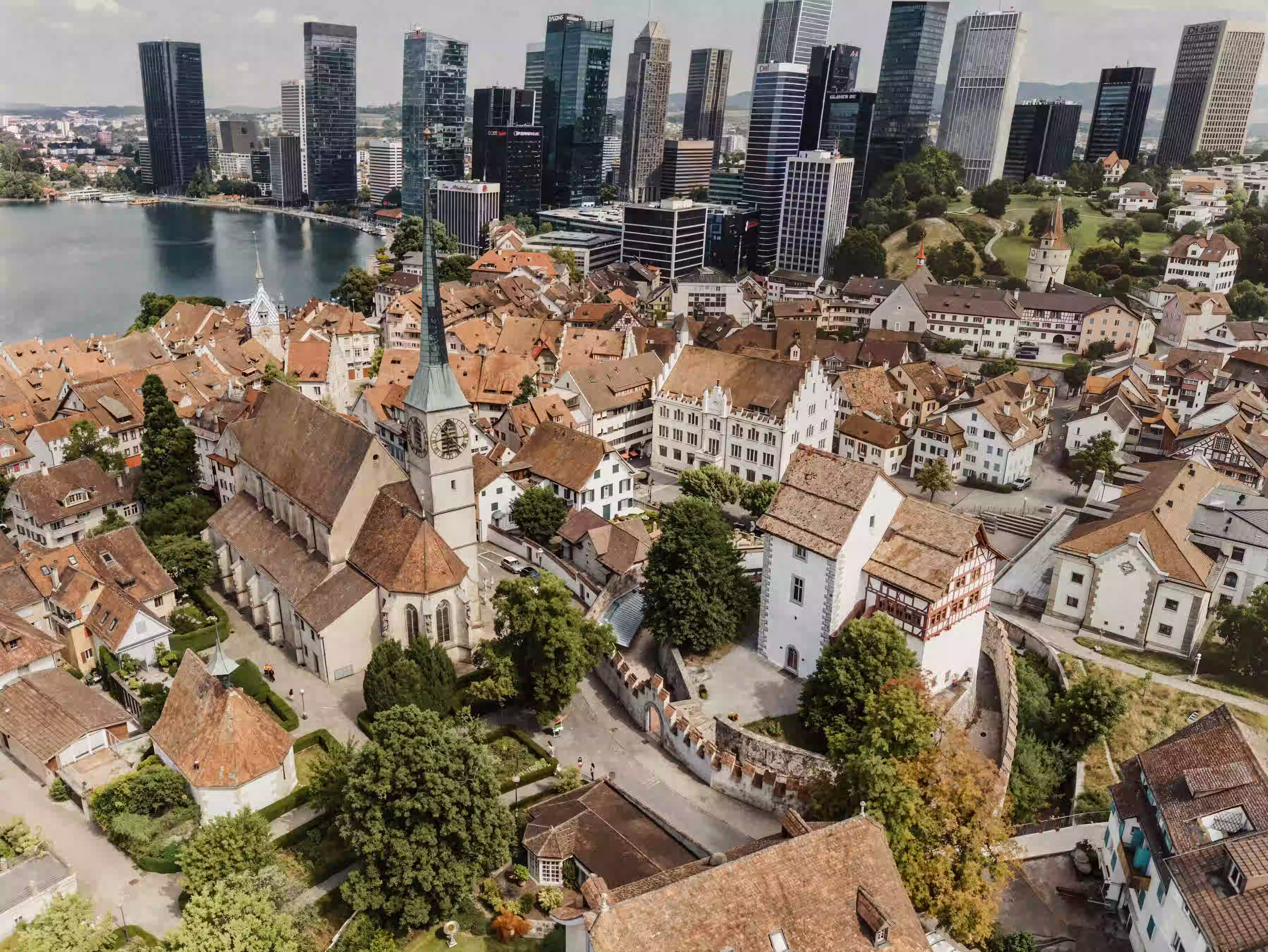 Luftaufnahme der Altstadt mit Kirche, historischen Häusern und modernen Wolkenkratzern am Seeufer.