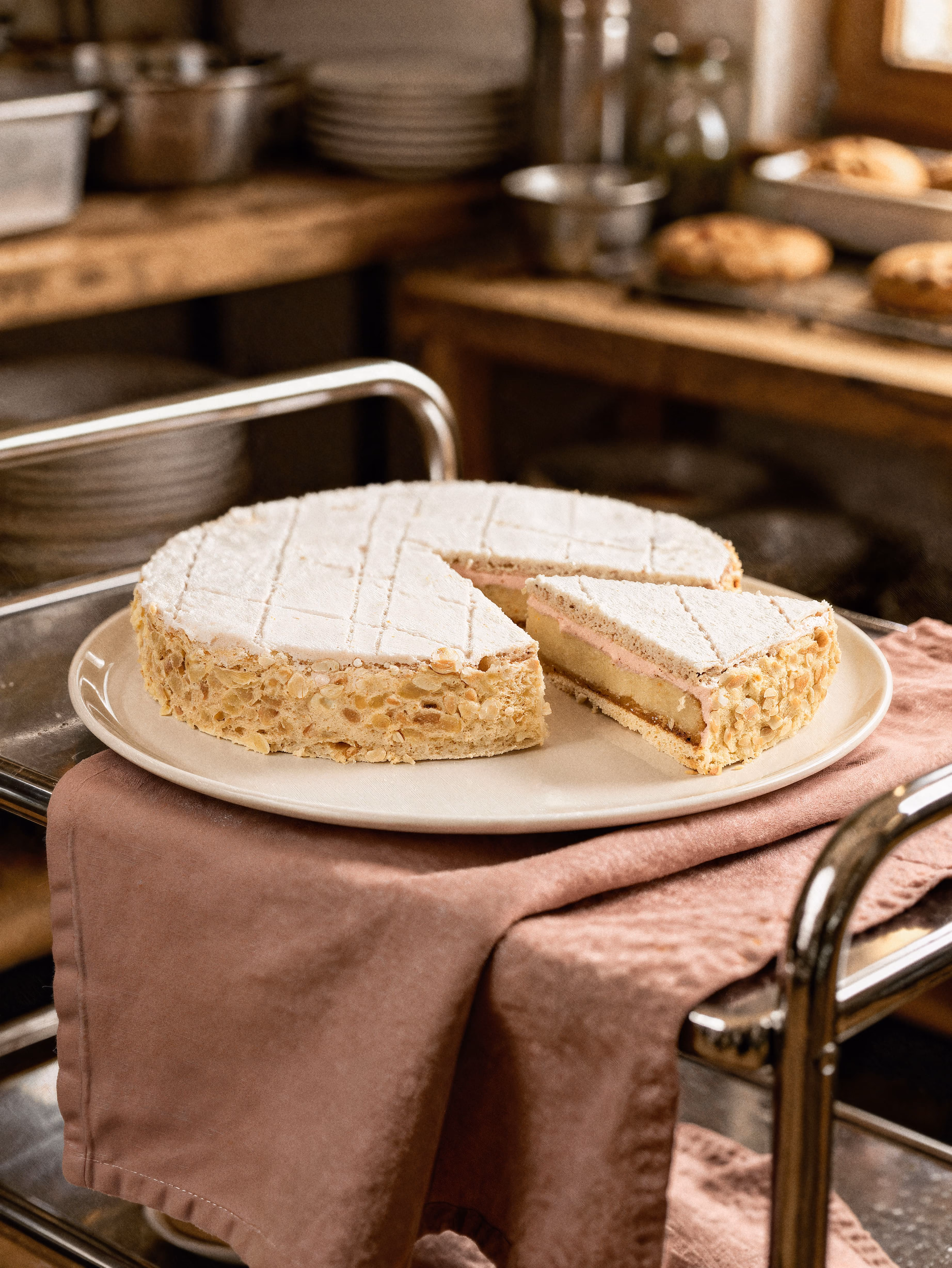 Zugertorte mit einer Scheibe auf einem Teller auf rosa Tuch auf einem Küchenwagen.