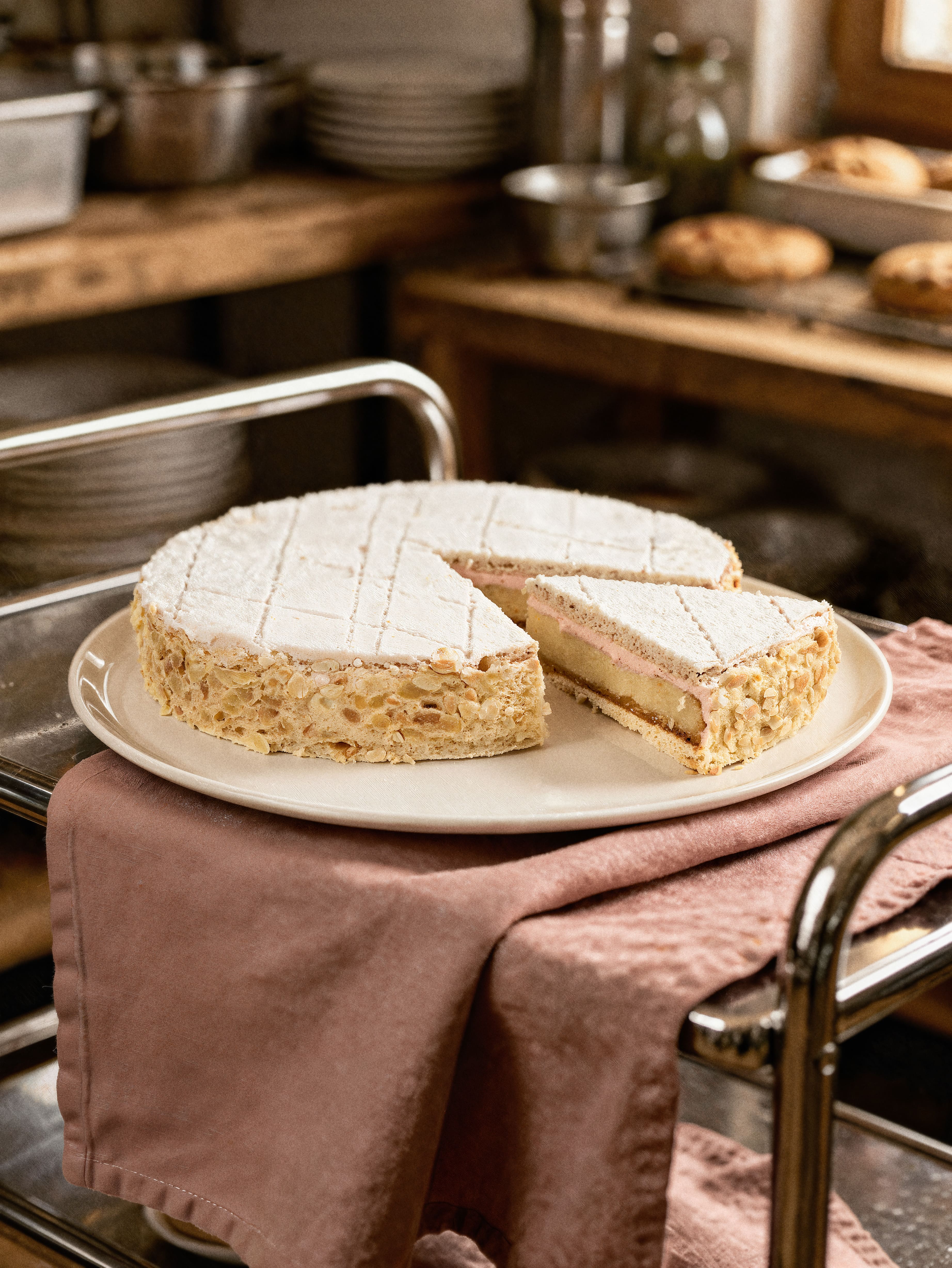Zugertorte mit einer Scheibe auf einem Teller auf rosa Tuch auf einem Küchenwagen.