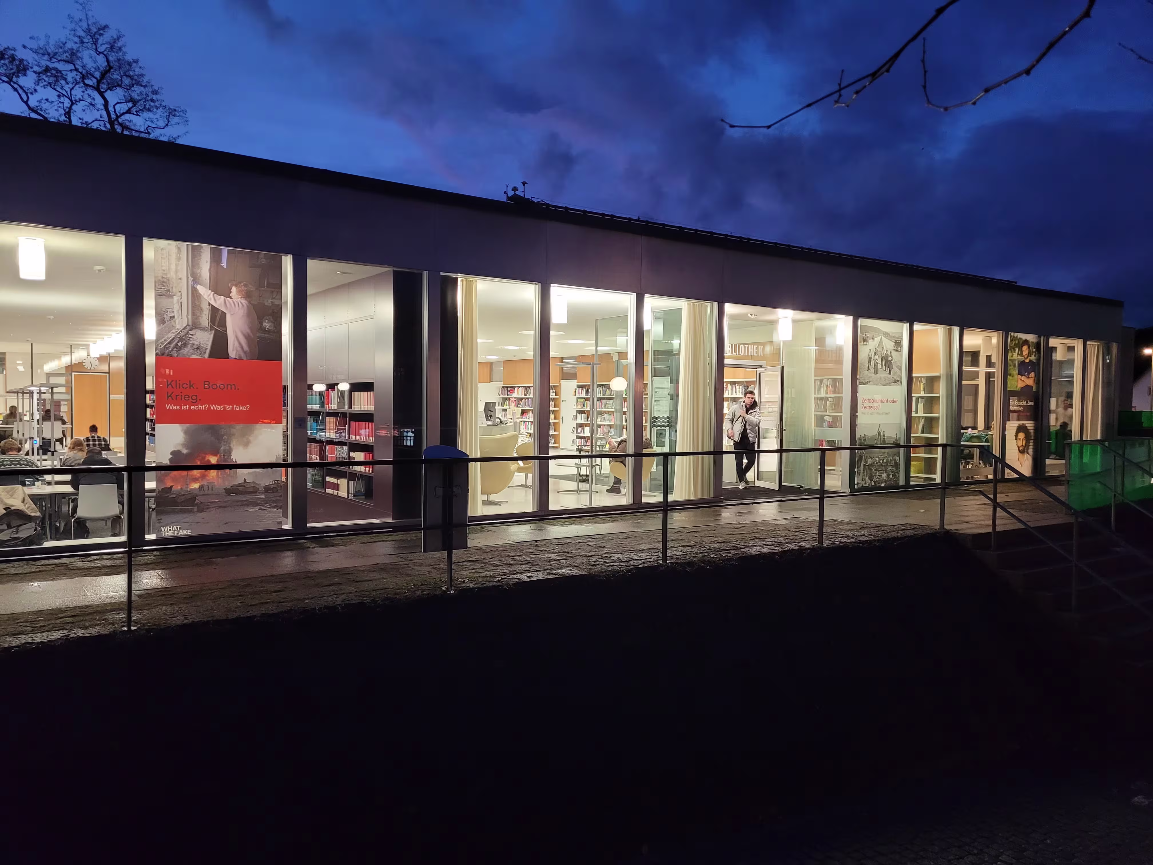 Bibliotheksgebäude mit beleuchteten Fenstern und Menschen darin bei Nacht.