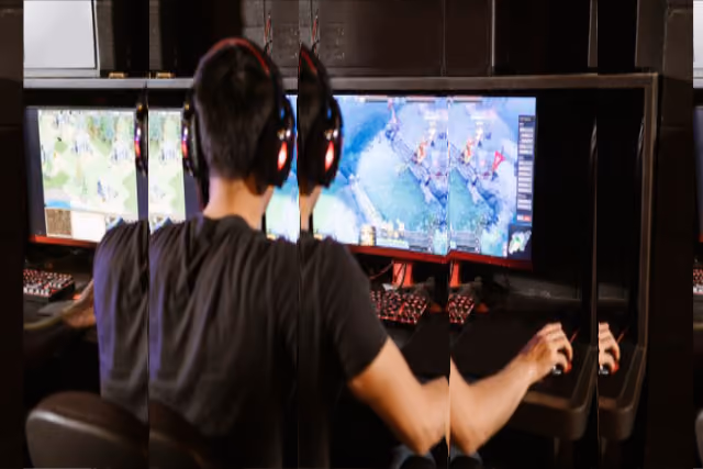 Person sitzt mit Kopfhörern und spielt ein Strategiespiel an drei Monitoren.