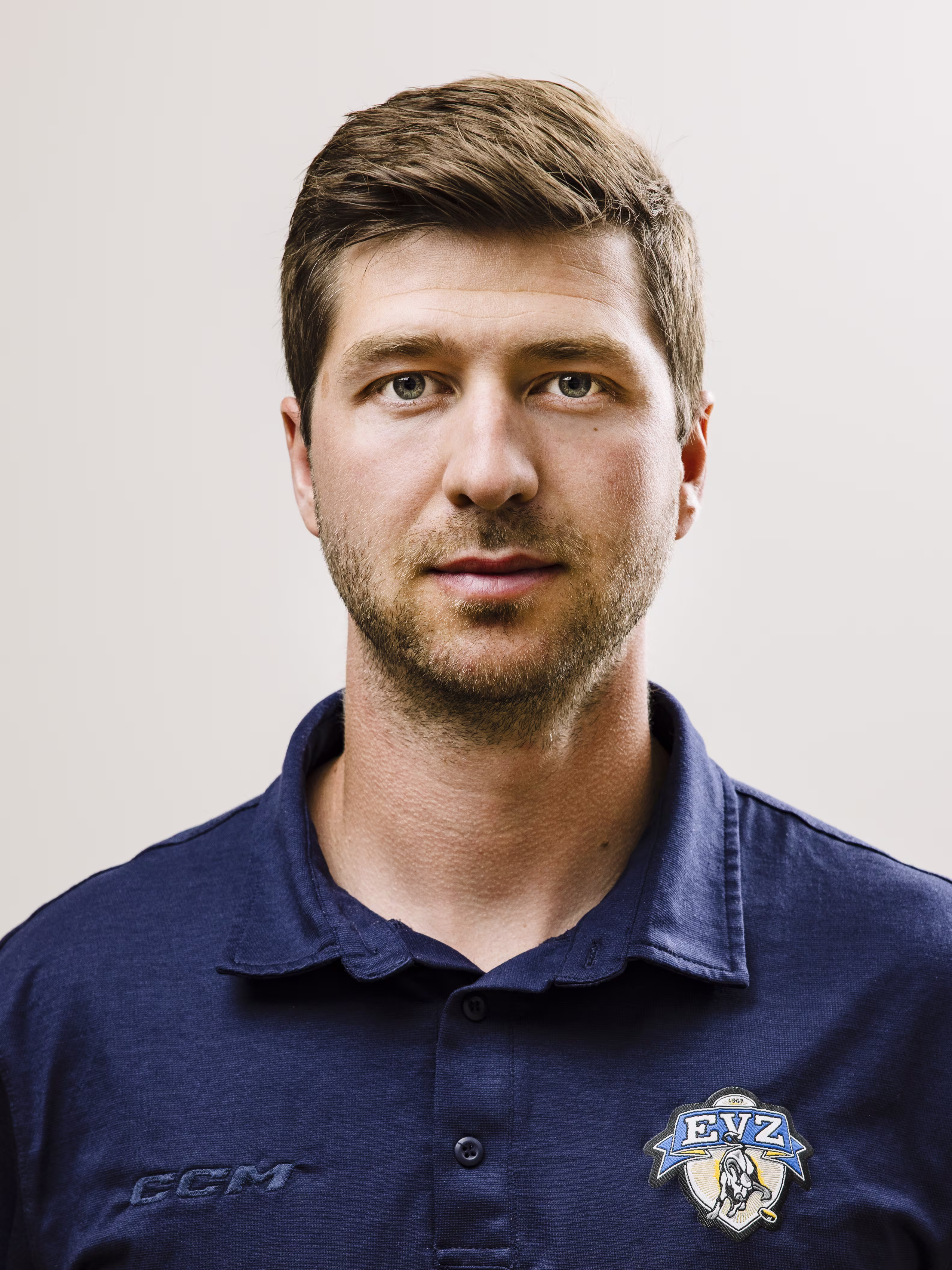 Porträt eines Mannes mit kurzem braunem Haar und Bart, der ein blaues Poloshirt mit EVZ-Logo trägt.