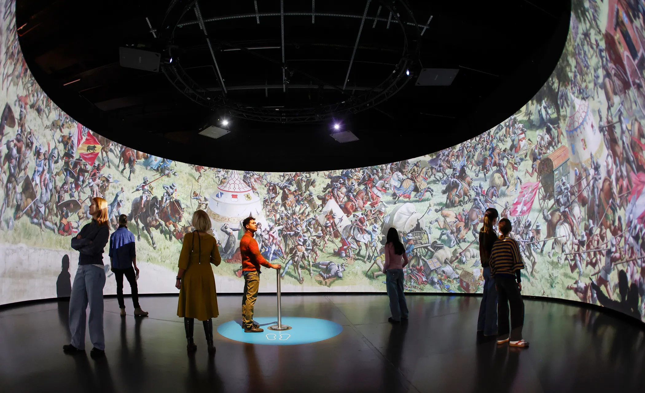 People watching a large, circular projection of a historical battle in a museum.