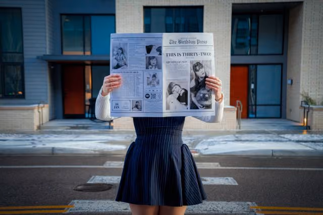 A woman holding a newspaper with a picture of a girl on it.
