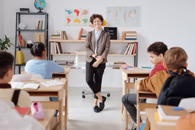 Teacher smiling in front of a classroom with students at desks, classroom scene.