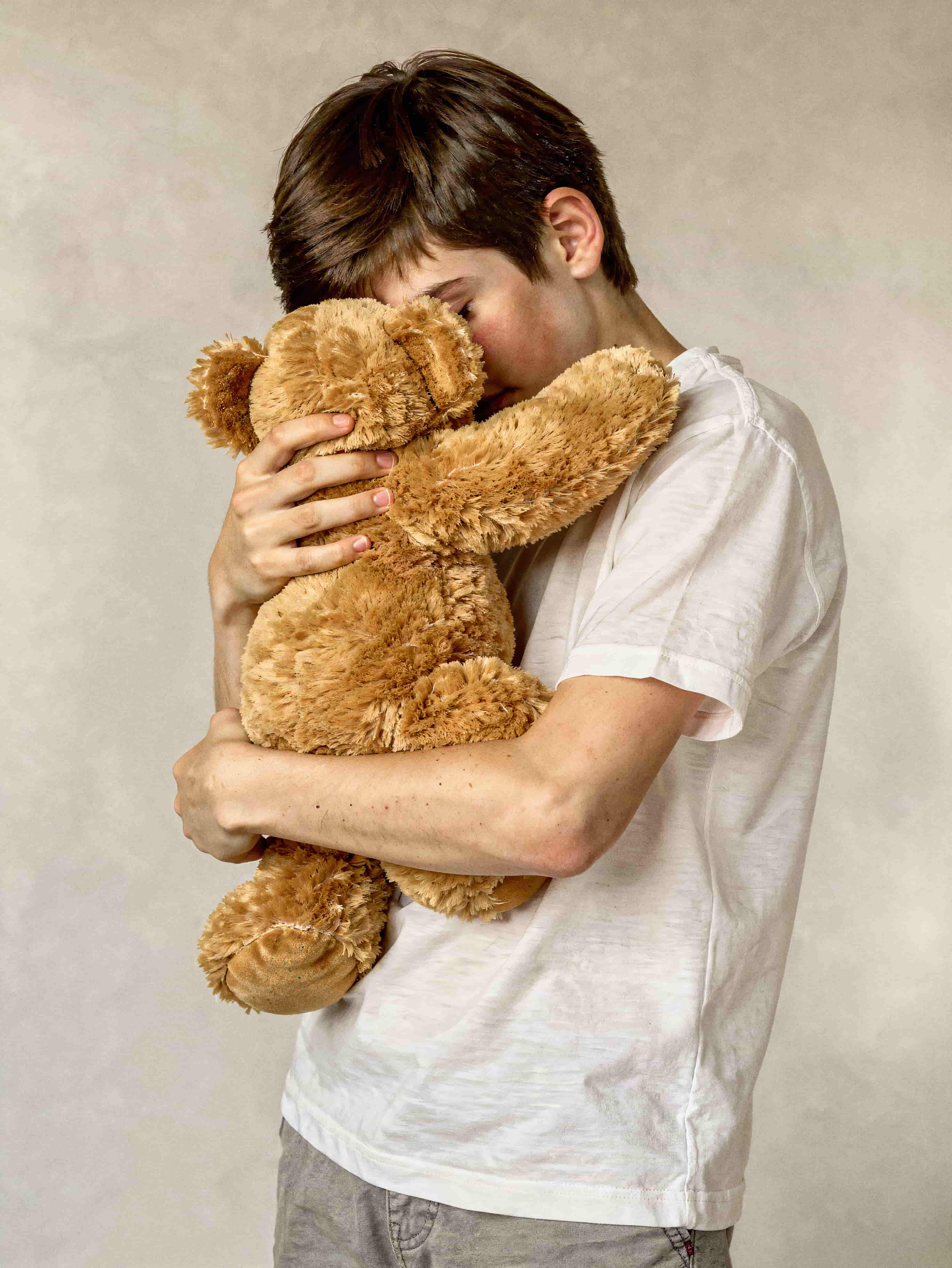 Junge drückt traurig einen braunen Teddybär eng an sich.