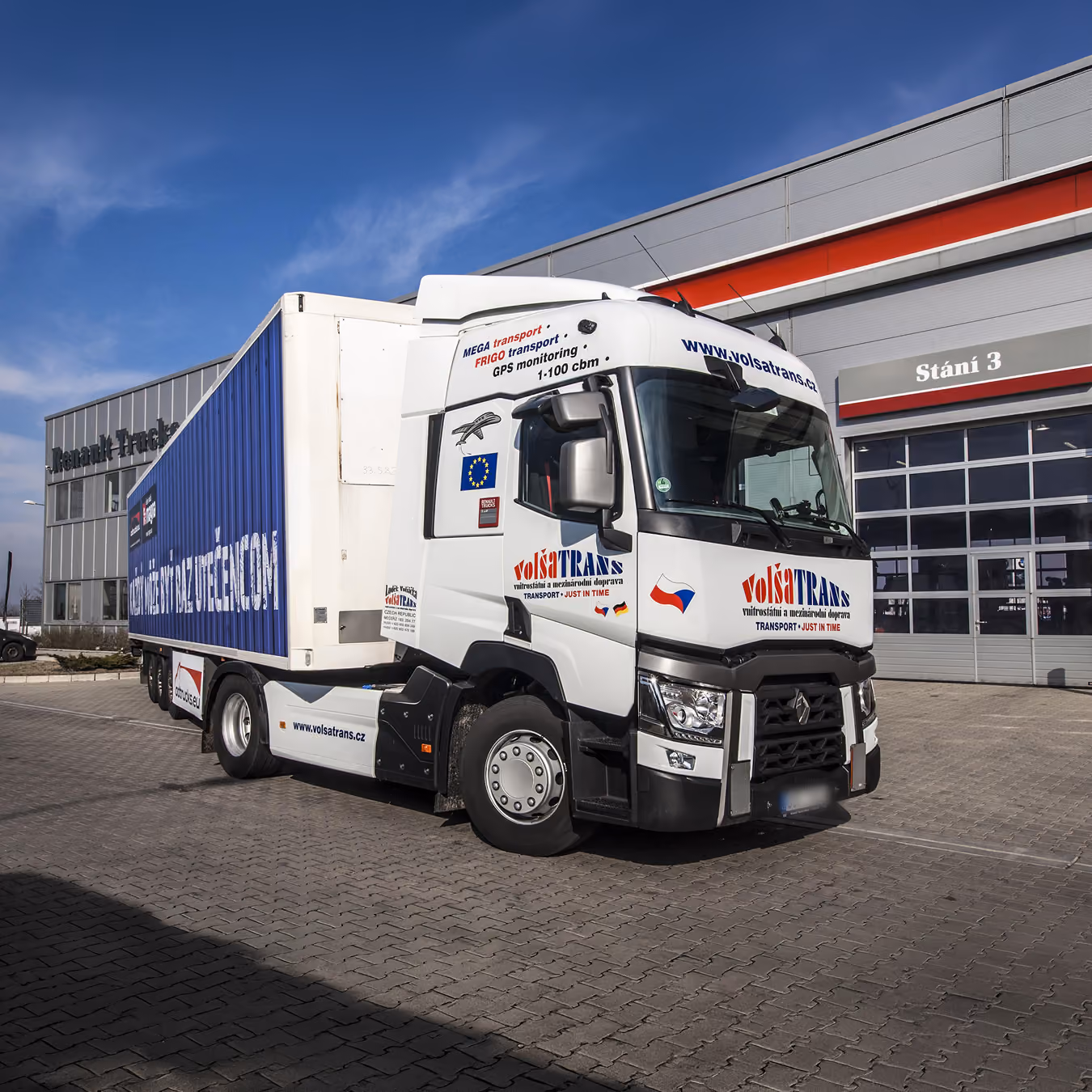 Bílý kamion VolšaTRANS s modrým návěsem zaparkován před budovou Renault Trucks.