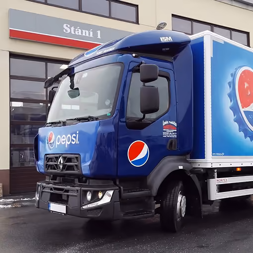 Nákladní vůz s modrým nátěrem a logem Pepsi před budovou s garážovými stáními.