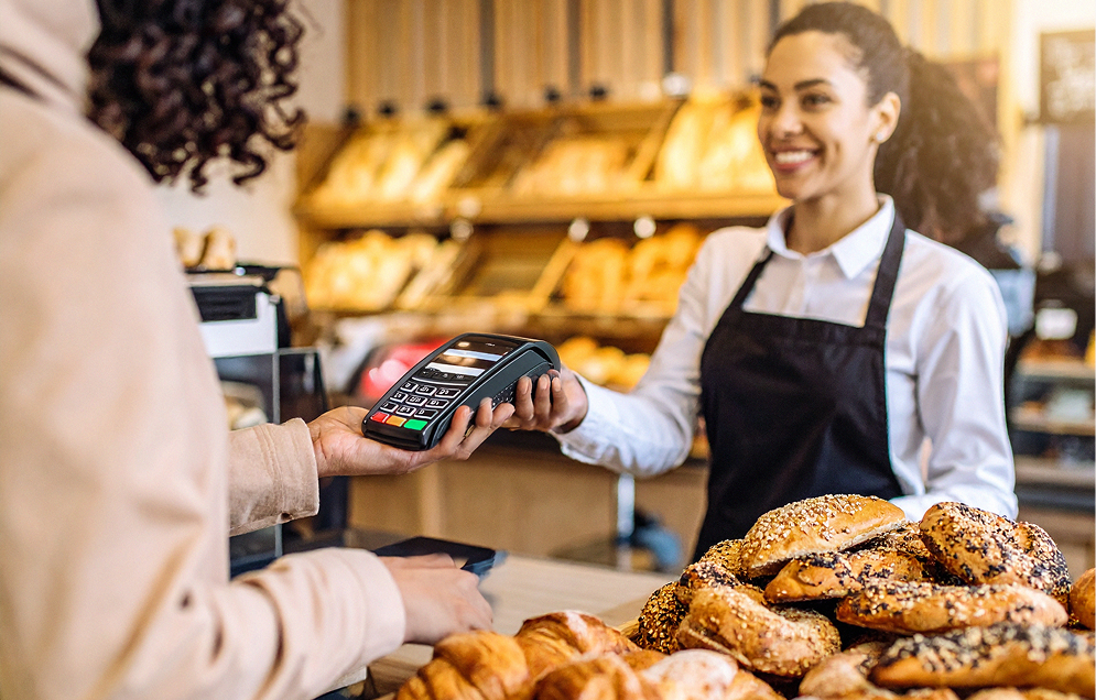 Woman in light-colored jacket scanning a card at a self-checkout machine in a modern clothing store.
