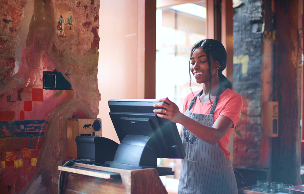 Pharmacist standing behind a counter with a dispensing machine and computer screens in a pharmacy.