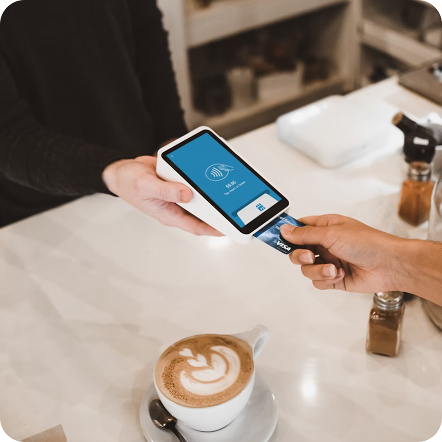 Customers in line at a modern bakery counter with a smiling male baker behind a glass display of croissants and pastries.