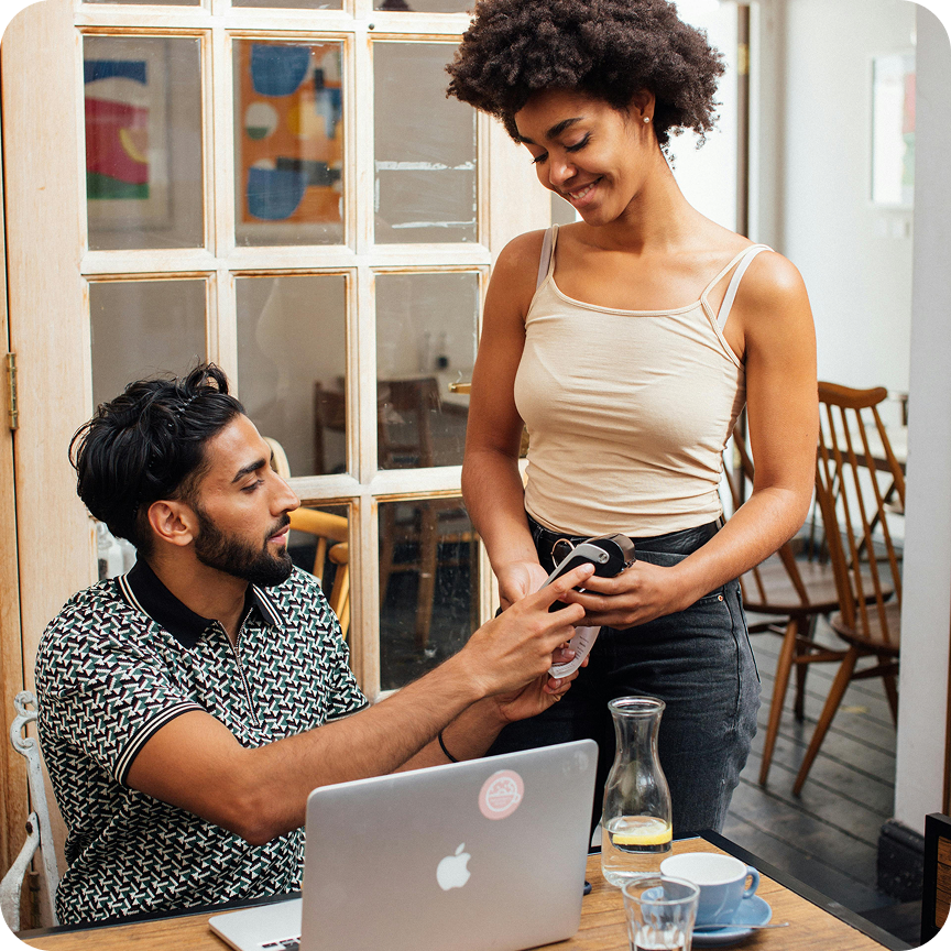 Customers in line at a modern bakery counter with a smiling male baker behind a glass display of croissants and pastries.