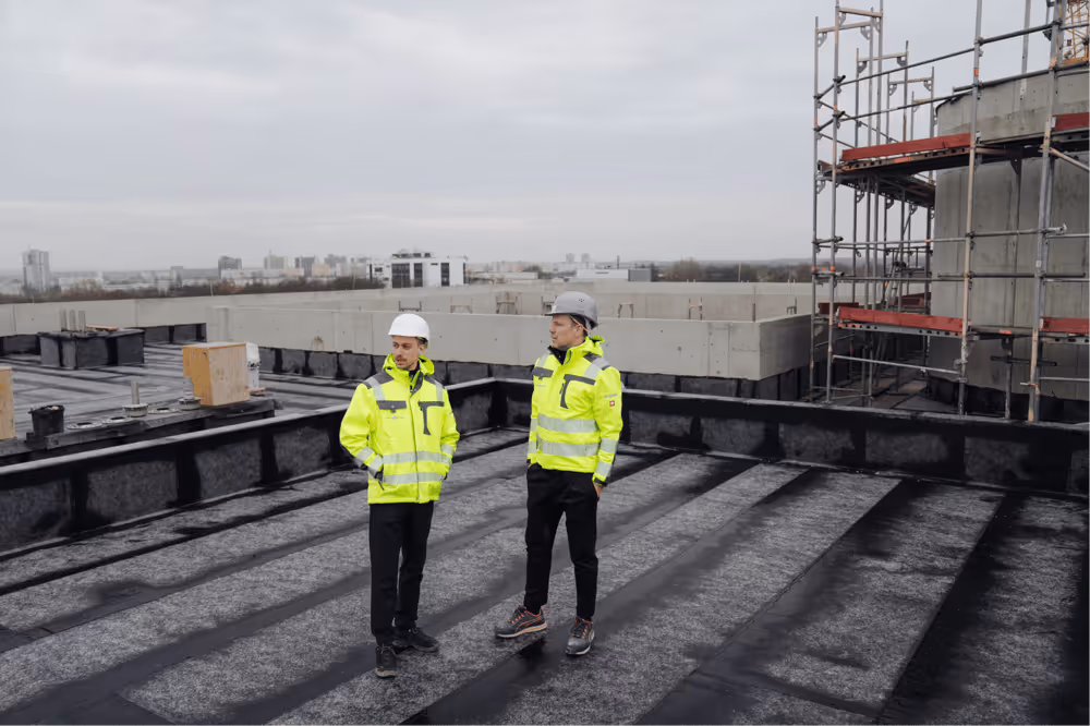 Zwei Kollegen in Sicherheitskleidung auf dem Dach einer Baustelle