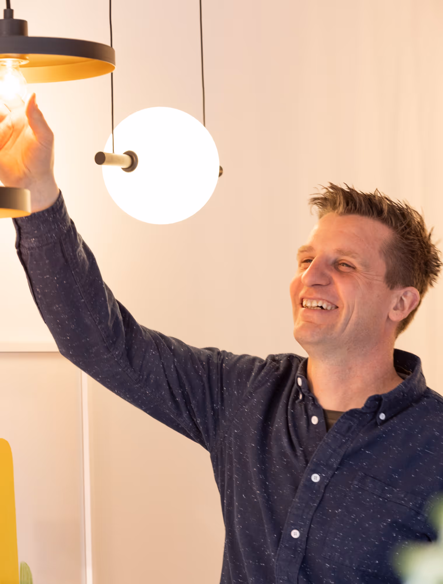 Een man in een donkerblauwe blouse draait een lamp vast.