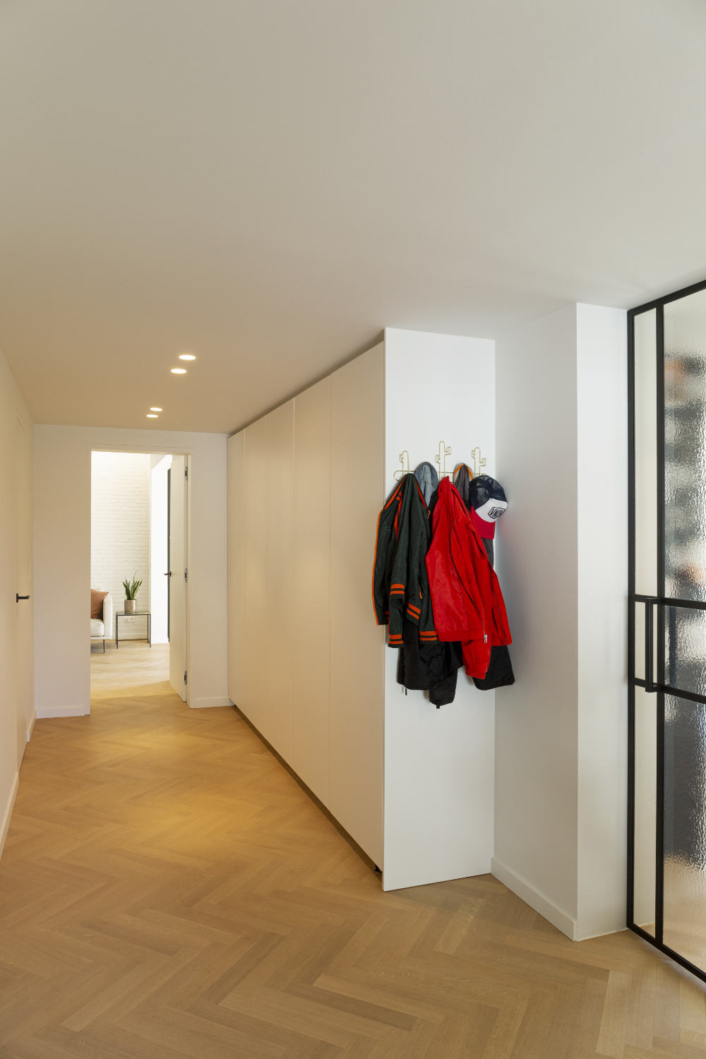 Een gang met witte muren, kapstok, en een glazen deur