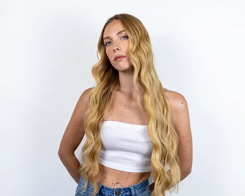 Ragazza con lunghi capelli biondi a onde morbide, top bianco e jeans su sfondo bianco