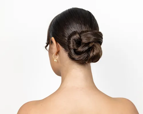 Chignon basso e liscio su capelli castani, visto da dietro su sfondo bianco