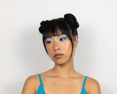 Ragazza con ombretto azzurro, frangia e due chignon alti, top azzurro