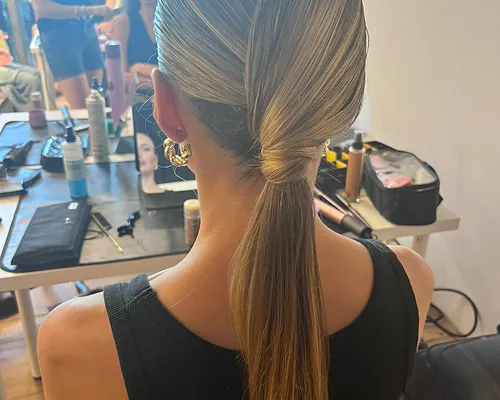Coda bassa liscia e ordinata su capelli biondi, davanti a una postazione trucco