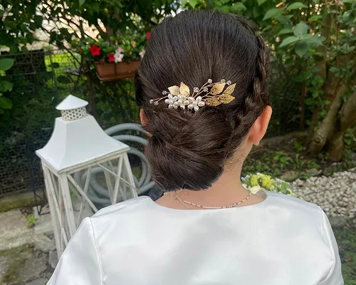 Chignon basso da sposa con fermaglio dorato a foglie e perle, visto da dietro in giardino