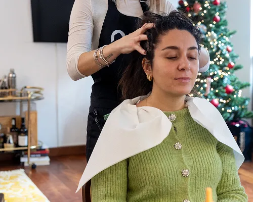 Parrucchiera Deeva acconcia una cliente con la mantellina in una casa addobbata per Natale