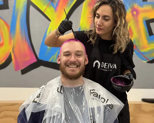 Colorista Deeva tinge di rosa i capelli di un ragazzo sorridente durante un evento con murales colorati