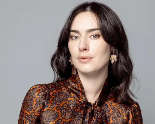 Donna con piega mossa su capelli castano scuro, camicia con fiocco e orecchini dorati