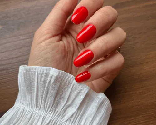 Mano con unghie a mandorla smaltate di rosso semipermanente, polsino bianco arricciato