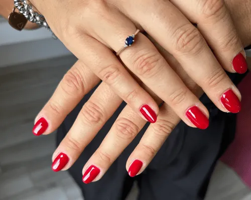 Mani con smalto rosso classico sulle unghie corte e un anello con pietra blu