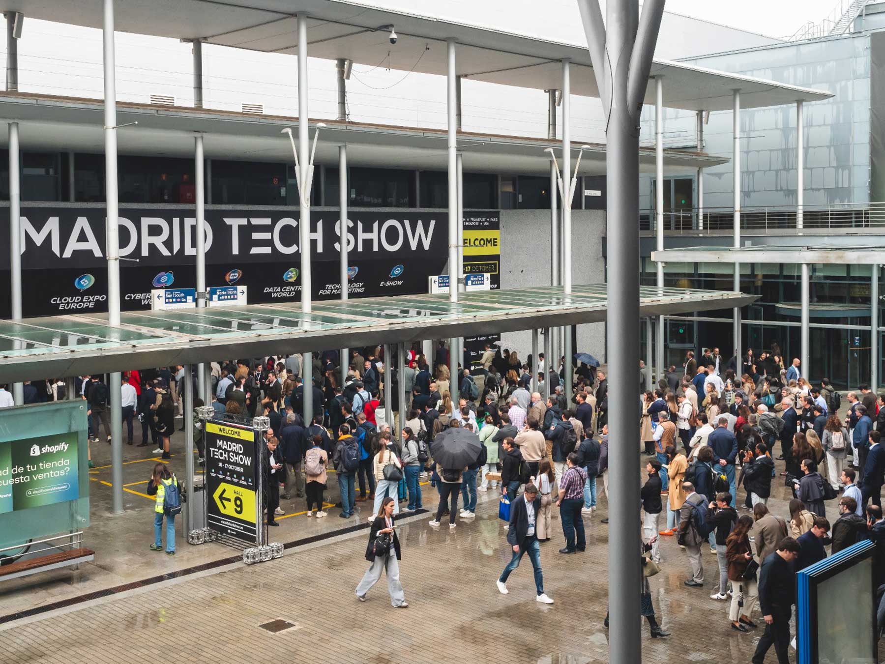 Crowd of people gathered outside a modern building under a covered walkway at Madrid Tech Show event.