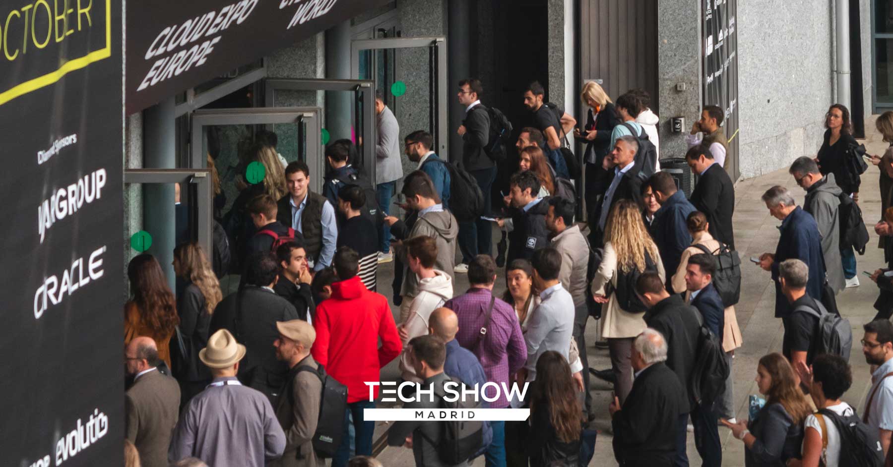 Crowd of people entering a building for Tech Show Madrid, with banners showing sponsors like VANGROUP and ORACLE.