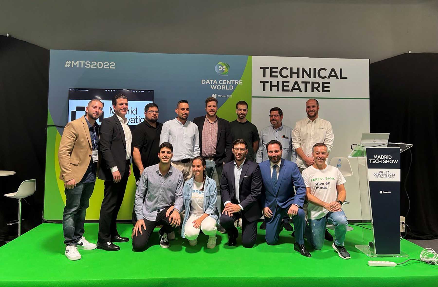 Group of twelve people posing on a green stage in front of a backdrop reading 'Technical Theatre' and 'Data Centre World' at Madrid Tech Show 2022.