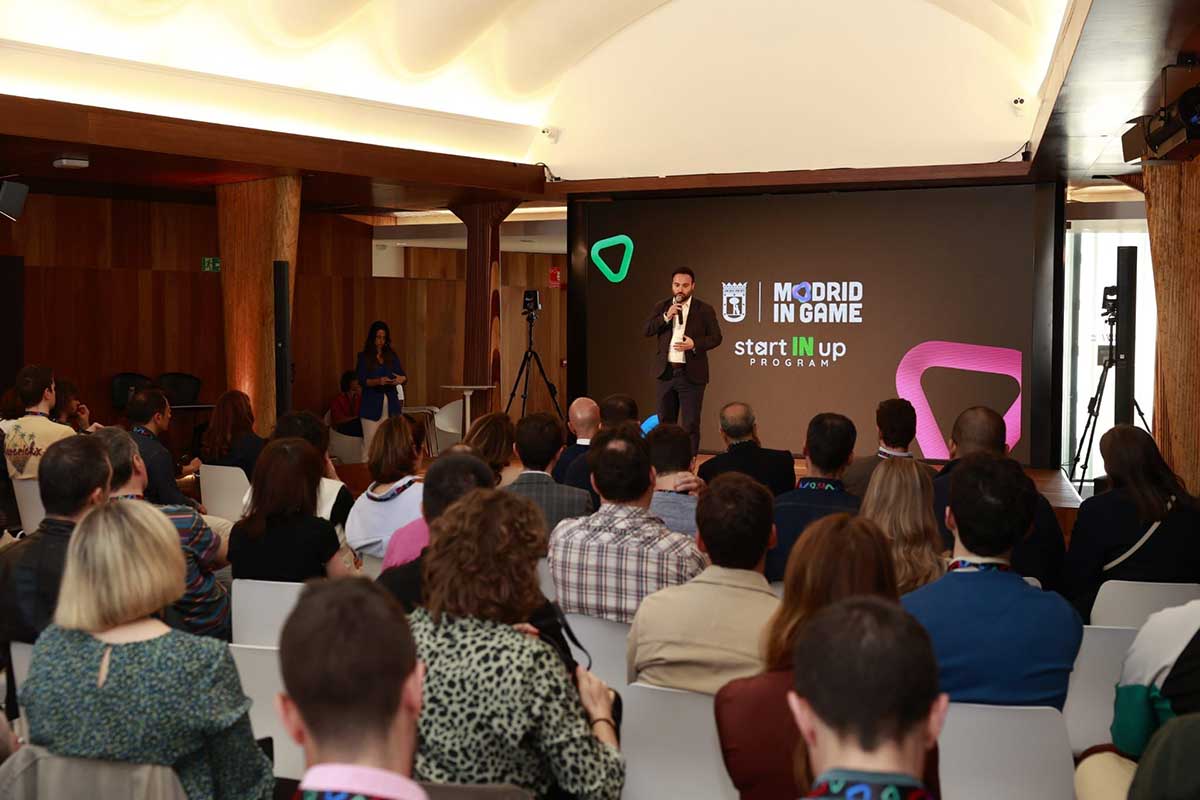 Audience seated facing a speaker on stage presenting at the Madrid In Game startup program event.
