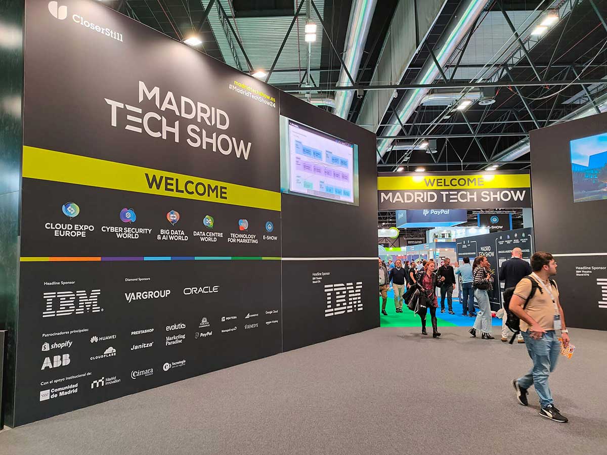 Entrance area of the Madrid Tech Show with welcome signs, sponsor logos including IBM, and visitors walking through the exhibition.