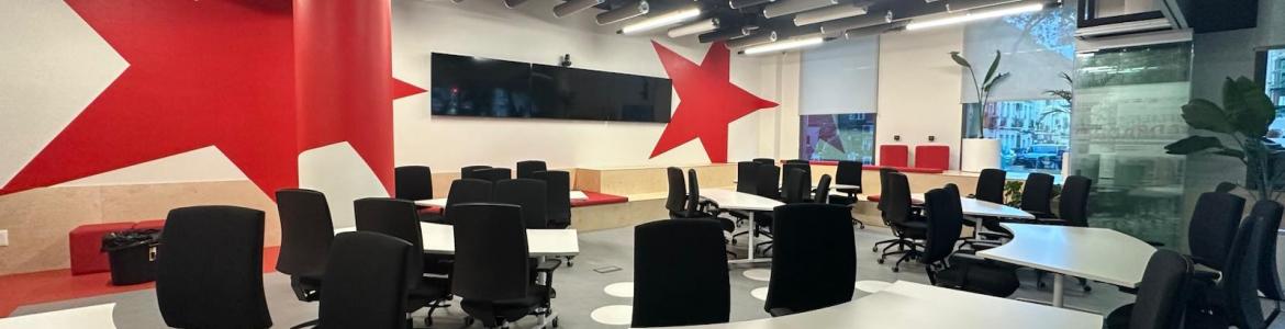 Modern conference room with multiple white tables, black office chairs, large red star wall decorations, flat-screen TV, and large windows.