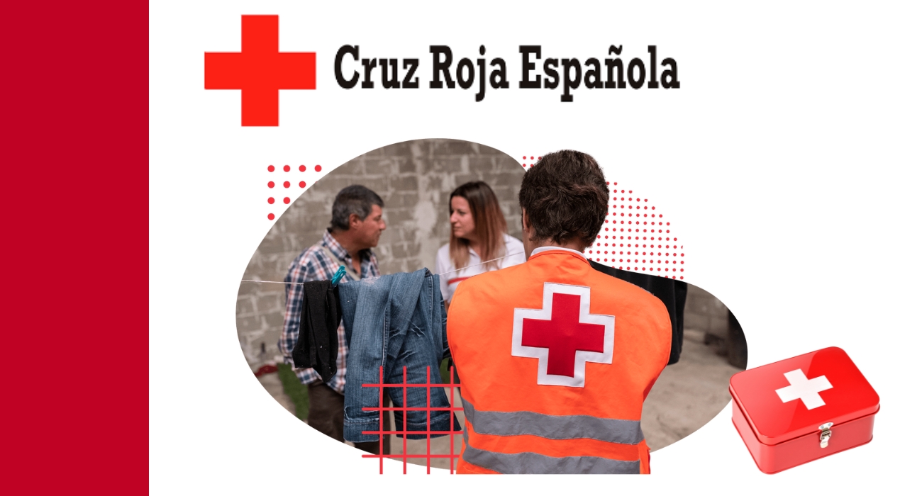 Volunteer in orange vest with red cross symbol facing two people talking near a wall, with a red first aid kit beside them, representing Cruz Roja Española.