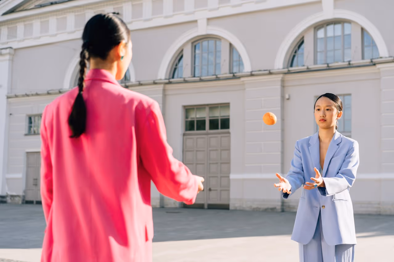 Two models wearing suits playing with an orange.