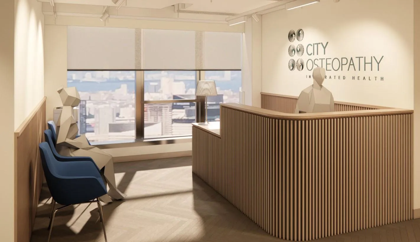 City Osteopathy clinic interior showing consultation area with blue treatment chair, wooden reception desk, and large windows overlooking Hong Kong cityscape at Chinachem Hollywood Centre location