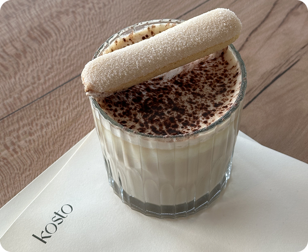 Creamy dessert topped with chocolate shavings and a ladyfinger, served in a glass on a Kosto napkin.