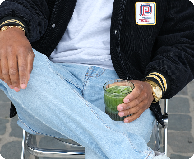 Seated guest holding a matcha drink, wearing a black jacket and light blue jeans.