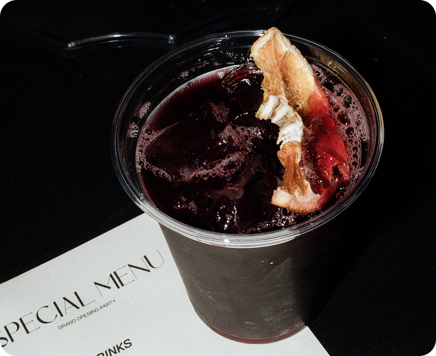 Iced drink topped with citrus peel and dark syrup, served on a branded Kosto napkin.