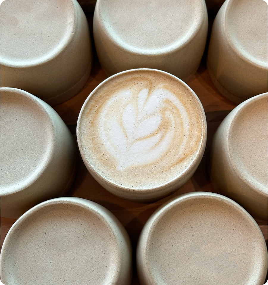 Top view of a group of ceramic coffee cups, one filled with a flat white and latte art.
