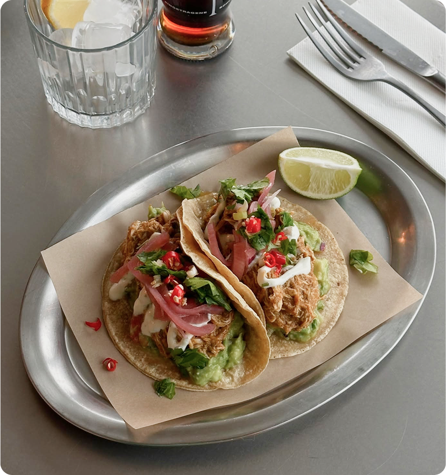 Plated tacos with lime, pomegranate seeds and herbs, served on a silver tray.