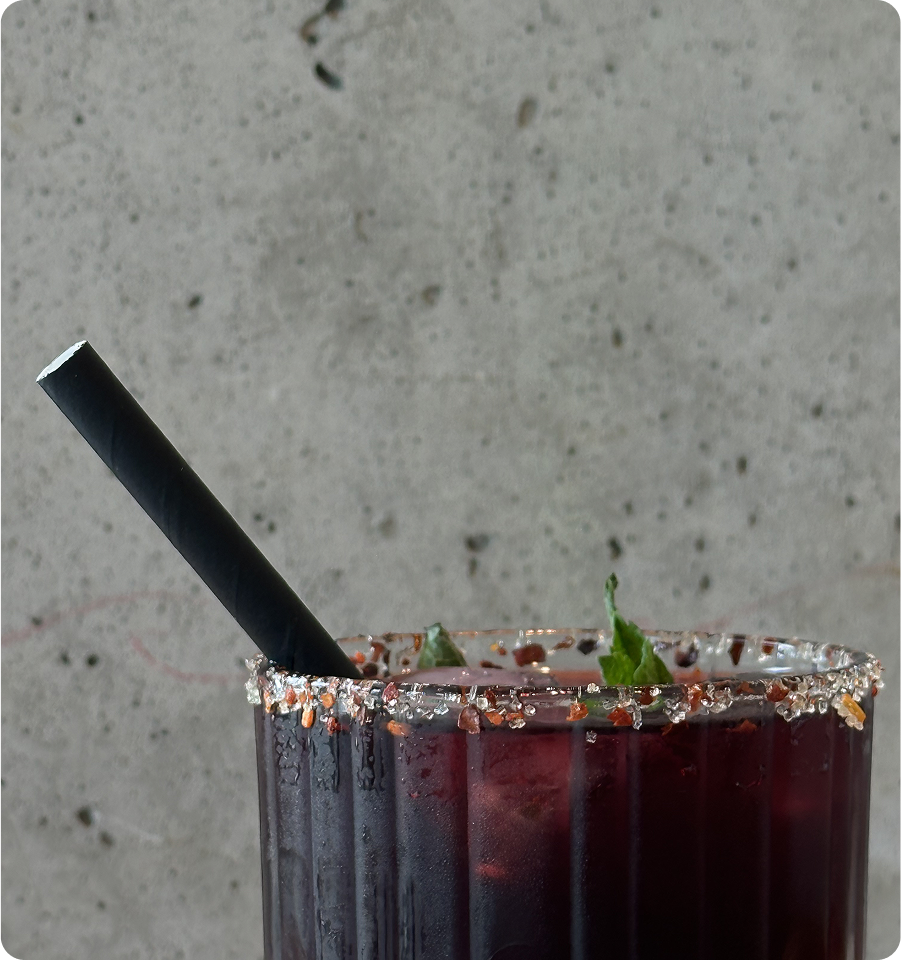 Dark cocktail served in a glass rimmed with salt and topped with fresh herbs.