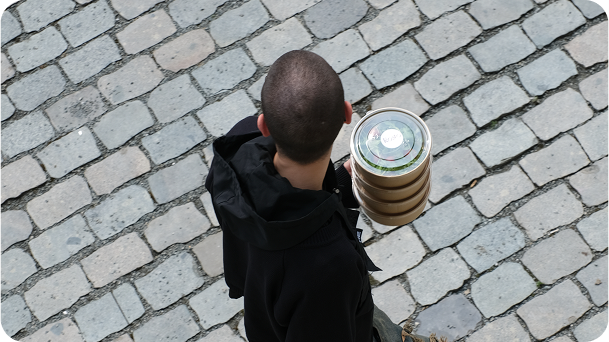A person walking on cobblestone streets holding a stack of takeaway cups from above.