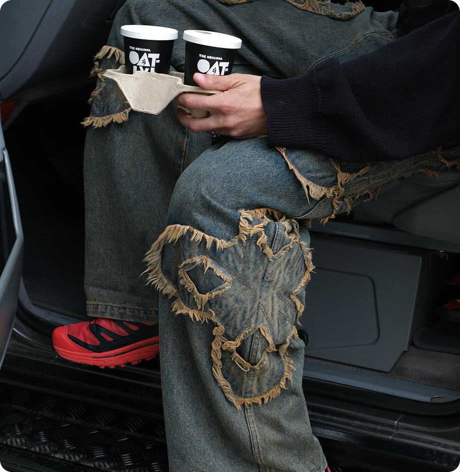 a man holding two take away coffees sitting in his car